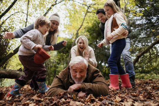 Grandfather playing in autumn leaves with family in forest