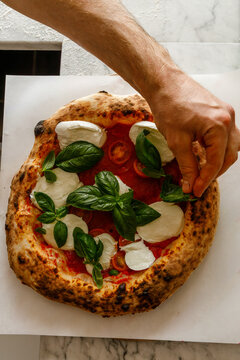 Pizzaiola decorates the finished pizza with a basil leaf
