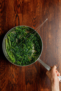 Chef holding frying pan with fried asparagus and spinach