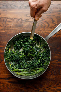 Chef holding frying pan with fried asparagus and spinach