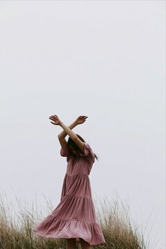 Woman in pink dress with arms crossed outdoors