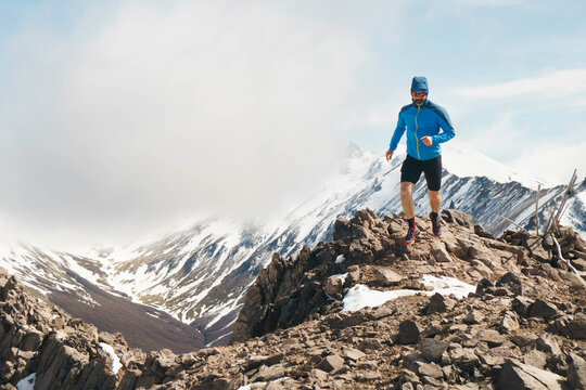 Trail runner at a rocky ridgeline with snowy mountain peaks
