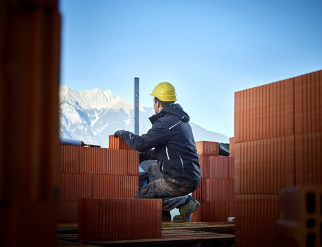 Bricklayer using spirit level on stacked bricks crouching at construction site