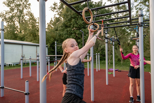 Young girl with braids trains on outdoor gym rings