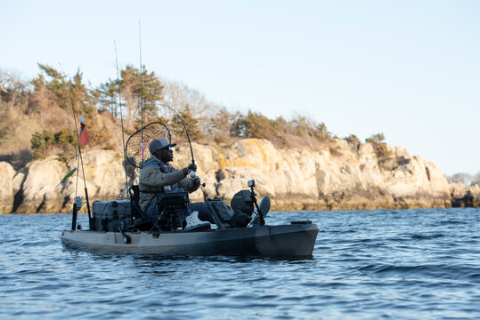 Man kayak fishing along a rocky coastline
