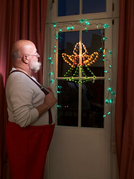 Santa standing by window looking at Christmas illumination at night