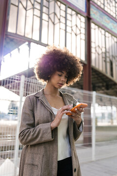 Cheerful woman with afro hairstyle using smartphone at train station
