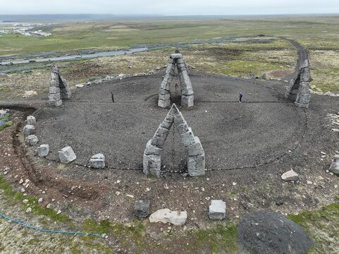 Aerial view of Arctic Henge, a stone monument with large archways arranged in a circle on a gravel landscape with people walking nearby in Raufarhofn, Nordurthing, Iceland.