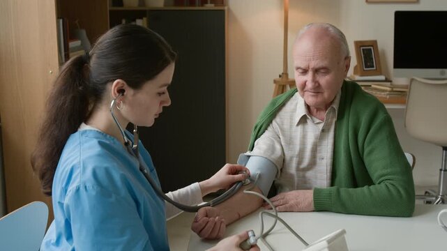 Young female nurse measuring blood pressure of senior man using manual sphygmomanometer. Clip for medical insurance and senior care advertising