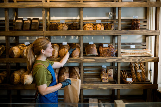 Shop assistant working in bakery selling artisan bread to customer