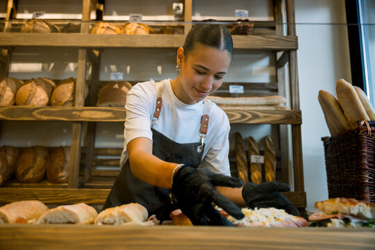 Trainee in bakery organizing pastries and bread behind the counter