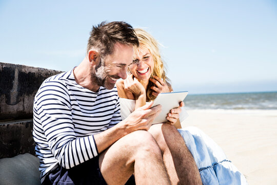 Happy couple on the beach looking at tablet