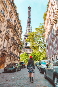 France, Paris, Eiffel Tower among the buildings, nearby street and woman wearing a red beret walking on the street