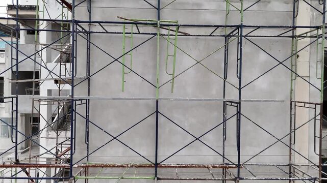 Drone Pullback from Scaffolding and Building Under Construction. Drone footage starting close to construction scaffolding before smoothly flying backward to reveal more of the unfinished building.