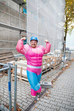 Portrait of a proud man wearing pink bodybuilder costume and hard hat at construction site