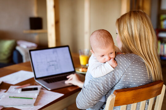 Mother with baby at home using laptop