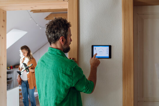 Man adjusting temperature through app on tablet PC in attic at home