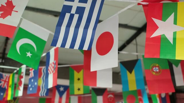 International Flag Bunting Waving in the Wind. Rows of colorful international flags gently move in the wind, creating a festive and multicultural atmosphere. The footage features recognizable national