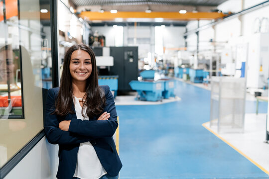 Confident woman working in high tech enterprise, standing in factory workshop with arms crossed