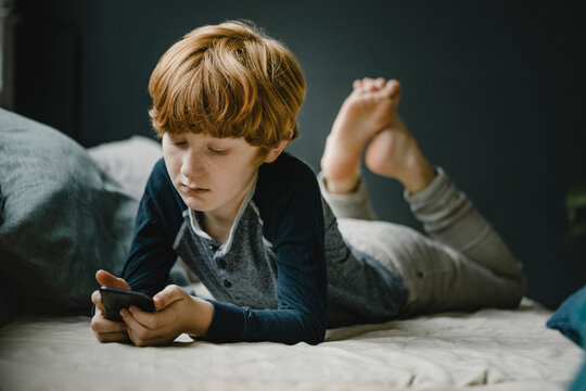 Portrait of redheaded boy lying on couch looking at mobile phone