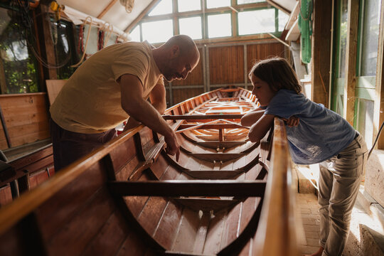 Father and son working together on wooden boat in sunny workshop