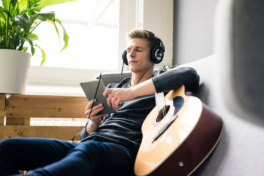 Relaxed young man with tablet and guitar listening to music with headphones