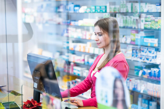Young pharmacist working on desktop PC at checkout counter