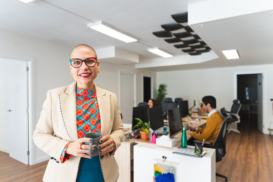 Smiling bald businesswoman holding mug in modern startup office
