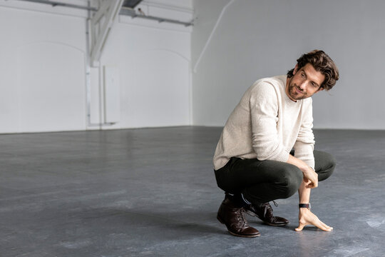 Smiling businessman crouching in industrial hall