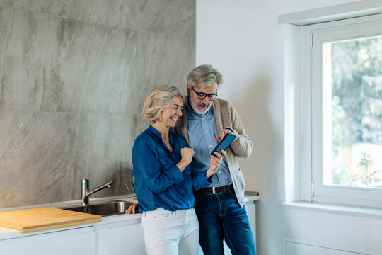 Mature couple using cell phone together in kitchen at home
