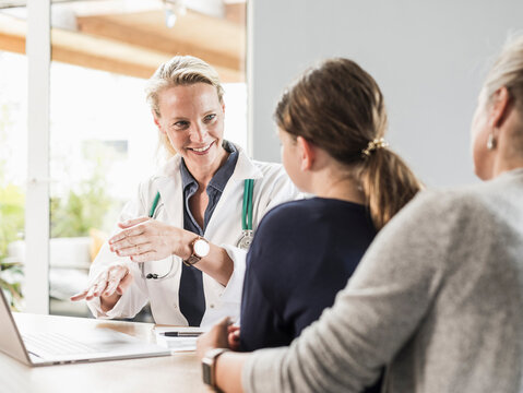 Smiling doctor giving advice to patient and woman at office