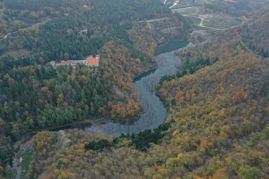 Aerial view of Lago di Poggio Baldi surrounded by dense autumn forests and winding river paths in Santa Sofia, Emilia-Romagna, Italy.