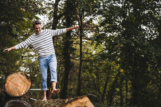 Cheerful mature man walking on log in forest