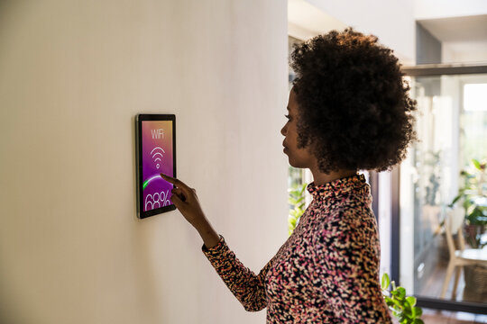 Homeowner adjusting smart home control panel on wall indoors