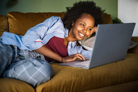 Smiling woman lying on sofa using notebook at home