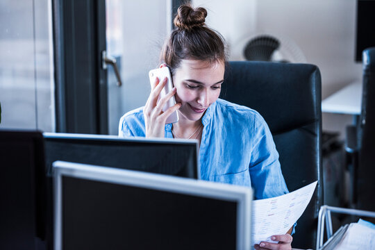 Businesswoman talking on mobile phone and reading document in office