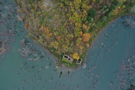 Aerial view of the ruins of a stone building on a forested peninsula surrounded by the submerged trees of Lago di Poggio Baldi in Santa Sofia, Emilia-Romagna, Italy.
