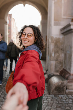 Smiling female tourist in red jacket leading by the hand on city street