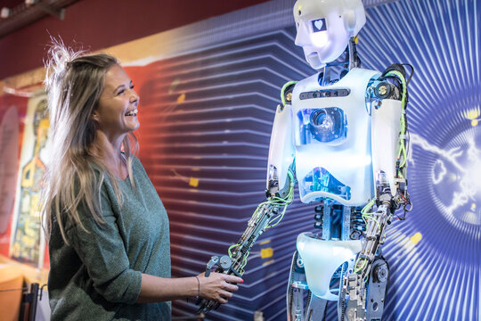 Happy technician shaking hands with human robot at workshop