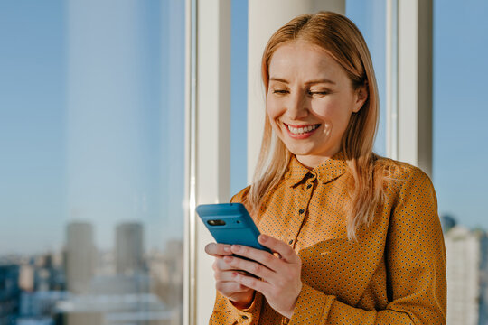 Smiling businesswoman messaging on phone near office window
