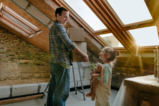 Father holding cardboard boxes near daughter in room under renovation