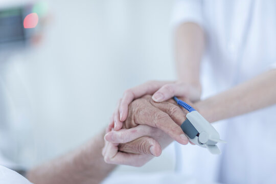 Finger heart monitor on patient, nurse holding hands