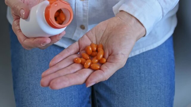 Close-up of orange vitamin capsules pouring from white plastic bottle into woman's hand. Concept of health, beauty and longevity. Daily supplementation, antioxidant coenzyme Q10, anti-aging and energy
