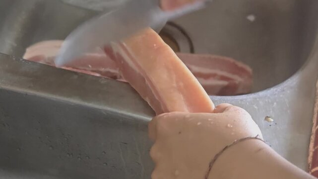 culinary chef or home cook preparing a thick slab of raw pork belly by meticulously scraping the pork skin rind with a sharp chef's knife