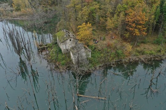 Aerial view of the abandoned stone ruins of Lago di Poggio Baldi surrounded by dead trees and calm water in Santa Sofia, Emilia-Romagna, Italy.