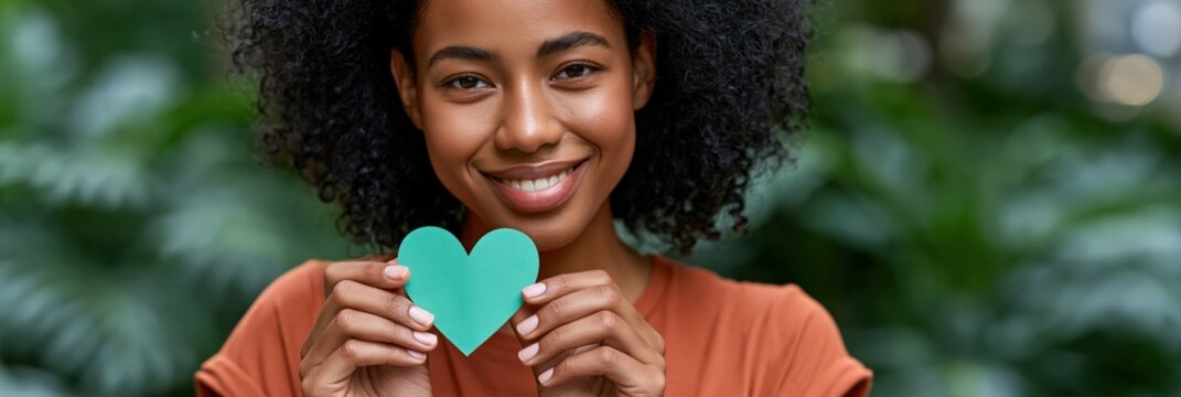 Smiling woman holding a green paper heart outdoors in nature for social banner and wellbeing campaign design