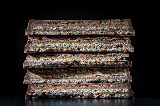 Stack chocolate wafer bars macro cross section. Macro close up of five chocolate covered wafer bars stacked vertically showing delicious crispy layers and cream filling isolated on black background
