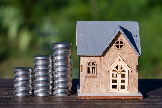 Wooden house model with growing stacks of coins. Miniature house model next to rising stacks of coins on wooden table representing real estate investment, mortgage savings and property market growth