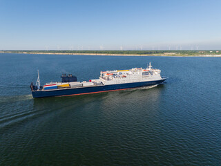 Fototapeta premium Aerial drone view of a Ro-Pax cargo passenger ferry ship sailing in the Baltic Sea near a coastline with wind turbines
