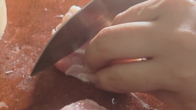 A high-quality macro close-up video capturing a person slicing and dicing fresh raw pork belly meat with a sharp chef's knife on a wet wooden cutting board.